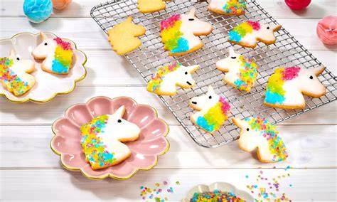 fröhliche bunte Einhorn-Kekse auf einem Teller, umgeben von Backutensilien und Verzierung