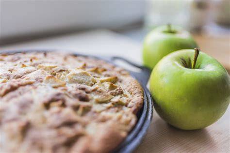 frisch gebackener Apfelkuchen auf einem Gitter, daneben frische Äpfel