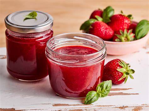 frische Erdbeeren in Gläsern, Marmelade und Obst auf einem Holztisch