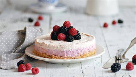 no-bake beeren-quarktorte auf keksboden, angeschnittenes stück, brombeeren-dekor